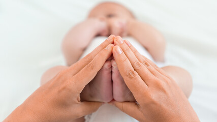Mother is holding a foots of the newborn on white sheet background. Mom and baby