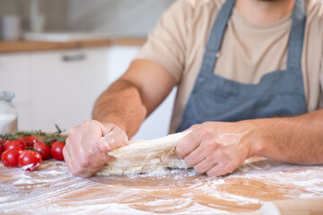 Baking concept. Unrecognizable male hands knead dough against the background of the kitchen. 