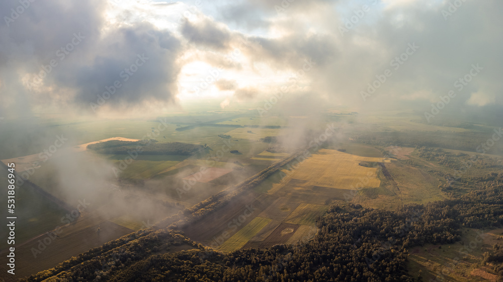 Sticker Flying high in the clouds over countryside. Aerial photo of clouds floating above countryside fields and forests, beautiful sunset from drone point of view