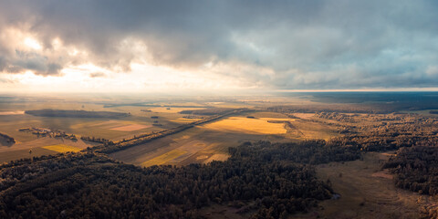 Dramatic aerial landscape of countryside with dark clouds, bright sun rays illuminating agricultural fields. Beautiful drone shot of sunset over fields