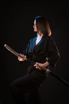 Portrait of young kung fu brunette girl with wakizashi on black background.