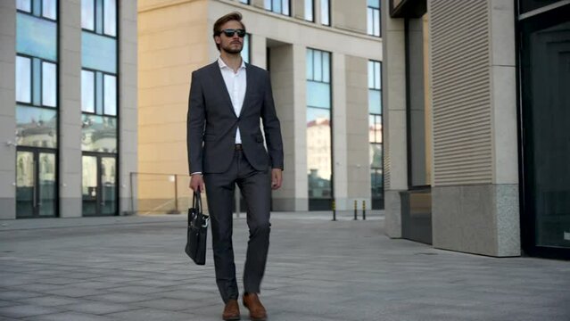 Successful confident stylish handsome caucasian businessman walking on street against background office building