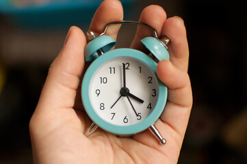 a small blue alarm clock showing 4 hours of time in your hand on a blurry background