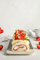 Plate with delicious strawberry roll cake on light background