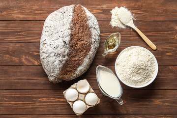 Loaf of bread, flour, oil, eggs and milk on wooden background