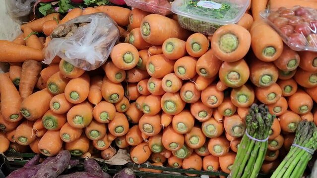 Video of many carrots in a food market. Carrots are stacked up. A few asparagus and other foods can also be seen. Recorded in 4k quality in 60 frames per second.