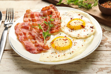 Plate with tasty fried eggs with bacon and spices on light wooden table, closeup