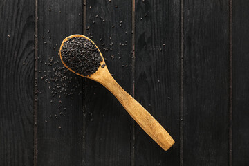 Spoon with black sesame seeds on dark wooden background