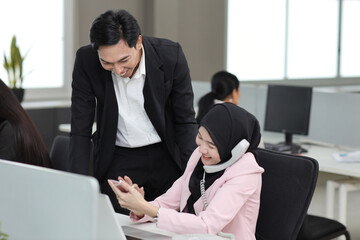 Attractive professional asian muslim female employee worker sitting, using laptop computer and calculator with coworker at workplace.Businesswoman talking on telephone and communicate with client.