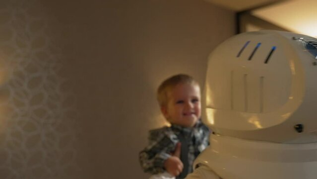 A mother in an astronaut costume spins her son in her arms. Games in a spaceship with a child in your arms in the interior of a cozy apartment.