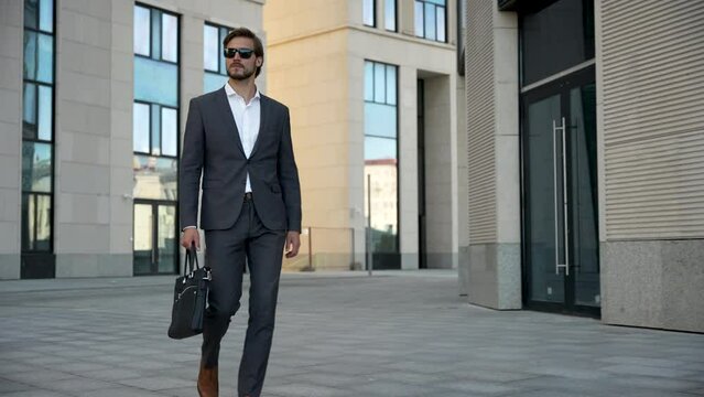 Successful confident stylish handsome caucasian businessman walking on street against background office building