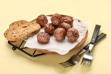 Stand with plate, meat balls, baking paper, forks and bread slice on beige background