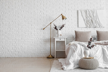 Interior of light bedroom with table, lamp and eucalyptus branches in vases