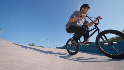 A professional cyclist rides and performs tricks on bmx. Beautiful stunts and bike jumps in the park on a concrete platform with obstacles. Man.

