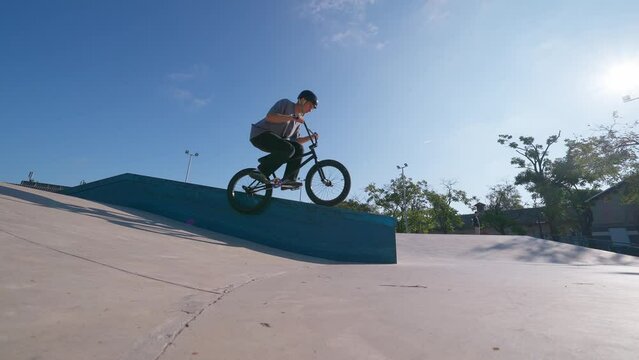 A professional cyclist rides and performs tricks on bmx. Beautiful stunts and bike jumps in the park on a concrete platform with obstacles.

