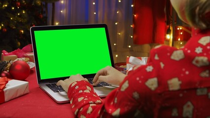 Back view of woman in red pajamas typing on laptop keyboard. Woman sitting at table near Christmas...