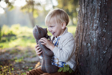 Uśmiechnięty chłopiec bawi się beztrosko w parku ze swoim misiem