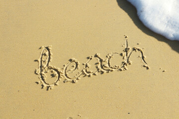 The word beach is written in the sand on a beach.