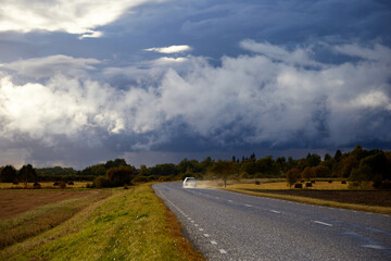 Landscape with a beautiful stormy sky full of clouds and a wet road with driving car