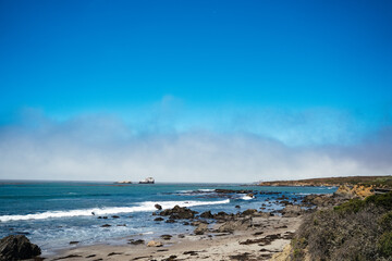 Pacific ocean beach with black rocks morning mist and blue sky. San Simeon vista point travelling along highway 101 California