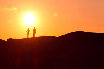 Silhouettes of two man against the setting sun. Two friends at sunset.