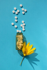 Vertical medical layout. On a blue background, a yellow flower and a bottle of pills. View from above. Allergy treatment. Medicines. Seasonal alegria.