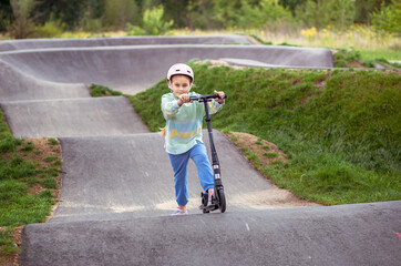  portrait of cute  little caucasian school girl wear helmet enjoy having fun riding  scooter on  asphalted track.in street park outdoors on sunny day. Healthy sport children activities outsid