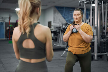 Caucasian plus size woman with her trainer working out in gym