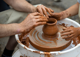 The potter teaches a young student. Hands of two people create pot on potter's wheel. Teaching traditional crafts.