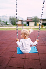 Little girl in a white tracksuit rides on a chain swing. High quality photo