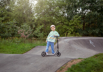  portrait of cute  little caucasian school girl wear helmet enjoy having fun riding  scooter on  asphalted track.in street park outdoors on sunny day. Healthy sport children activities outsid