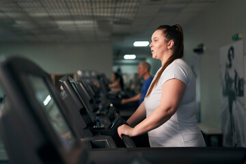 Fototapeta na wymiar Plus size caucasian woman running on treadmill at gym
