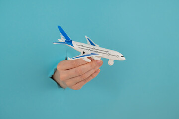 A female hand sticking out of a hole from a blue background holds a model of an airplane. 