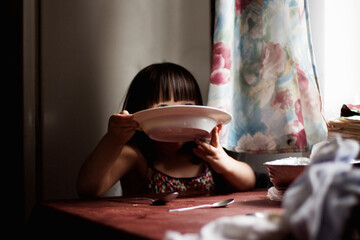 Głodne i biedne dziecko zjada talerz zupy i oblizuje się
