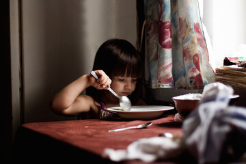 Głodne i biedne dziecko zjada talerz zupy i oblizuje się