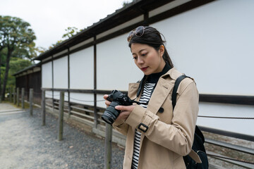 portrait of asian chinese girl visitor checking photos on her slr camera with concentration while visiting Motorikyu Nijyojo nijo castle in Kyoto japan