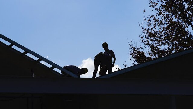 the dark silhouette of three workmen on the roof of a house under construction