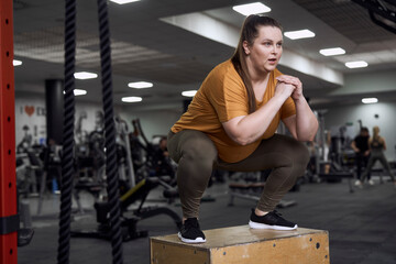 Woman with overweight jumping at the box in the gym