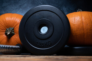 Heavy dumbbell barbell black weight plates with orange pumpkins. Healthy fitness lifestyle autumn...