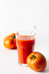 Homemade freshly squeezed tomato juice in a glass with a glass straw and tomatoes on a white background