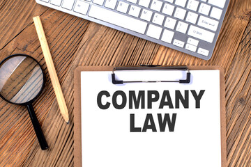 COMPANY LAW text on paper clipboard with magnifier and keyboard on wooden background