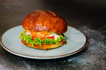 Top view of burger with shrimps, meat patty, salad, tomato against black background. Blue plate. Food lifestyle. Fast food. 