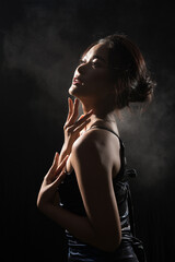Naklejka premium Portrait of Asian Woman in shadow low light key with back backlit, side rear view of female turn twist body for healthy shape fashion style. black background smoke exposure