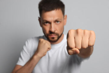 Naklejka premium Man throwing punch against grey background, focus on fist. Space for text
