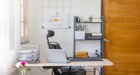 Laptop Computer, notebook, and eyeglasses sitting on a desk in a large open plan office space after working hours	