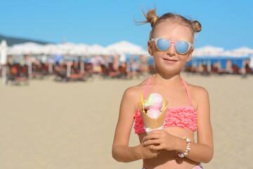 Adorable little girl in swimsuit with delicious ice cream at beach on sunny summer day, space for...