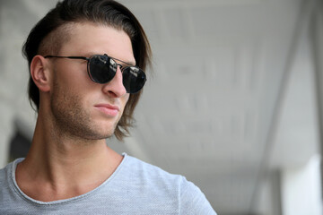 Portrait of handsome young man in stylish sunglasses indoors. Space for text