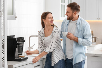 Happy couple preparing fresh aromatic coffee with modern machine in kitchen