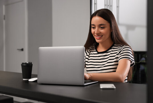 Happy young woman using laptop at table in hostel