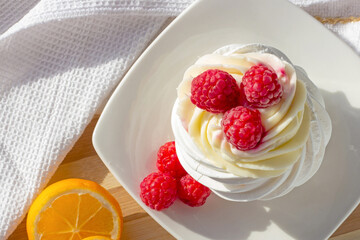 Top view of white mini meringue Pavlova cake with sweet pink raspberry berries and mascarpone cream on the plate in the kitchen.